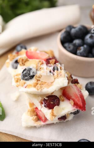 Morceaux d'écorce de yaourt savoureuse avec des baies et du granola sur la table grise, gros plan Banque D'Images