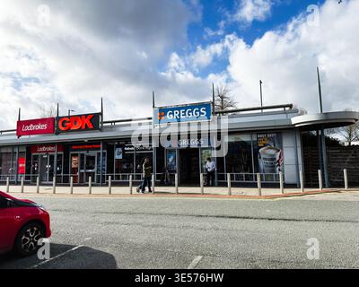 Manchester, Royaume-Uni - 22 février 2026 : boutiques incluant Greggs et Ladbrokes lors d'un défilé de Manchester avec piétons, signalisation et ciel couvert. Banque D'Images