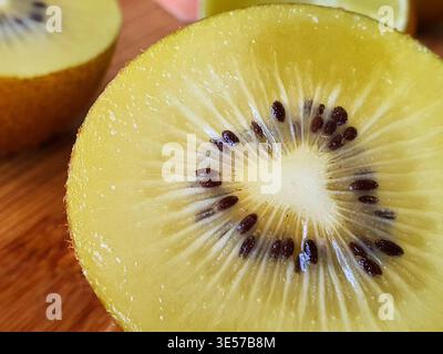 Macro-photographie en gros plan extrême d'un kiwi doré tranché (Actinidia chinensis) coupé en deux, révélant une chair jaune éclatante, un noyau radial blanc, Banque D'Images
