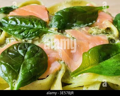 Macro-photographie en gros plan d'un plat de pâtes italiennes avec de larges nouilles en ruban enrobées d'une sauce verte crémeuse, surmontées de tranches de rose fumé Banque D'Images