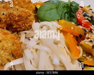 Gros plan macro d'un repas d'inspiration asiatique composé de côtelettes de poulet frites panées croustillantes accompagnées de nouilles de riz blanches, de légumes frais et de Banque D'Images