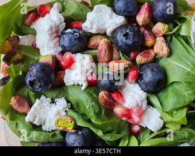 Vue rapprochée du ciel d'une salade fraîche composée de feuilles d'épinards vertes éclatantes surmontées de bleuets dosés, de graines de grenade rouge vif, décortiquées Banque D'Images