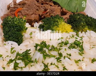 Une photographie rapprochée d'un repas préparé à l'asiatique servi dans un contenant jetable blanc. Le plat comprend du riz blanc moelleux garni de Banque D'Images