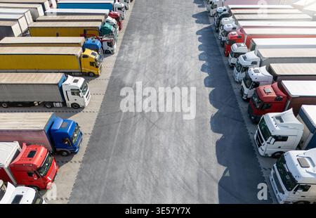 Vue aérienne d'un grand parking pour camions à un centre logistique, avec plusieurs semi-camions commerciaux stationnés en rangées organisées. Banque D'Images
