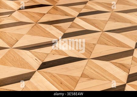 Parquet géométrique en bois avec panneaux triangulaires incrustés, tons bois clairs et sombres alternés et grain visible. Revêtement de sol texturé Banque D'Images