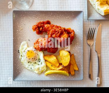 Pommes de terre cuites au four avec poulet dans la sauce et œuf frit sur l'assiette Banque D'Images
