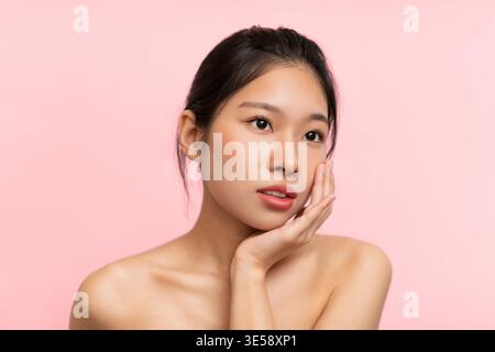 Jeune femme pose avec la main sur le visage contre fond rose pendant la séance de l'après-midi Banque D'Images
