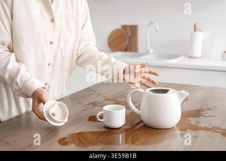 Femme avec tasse, pot et café renversé sur la table dans la cuisine Banque D'Images