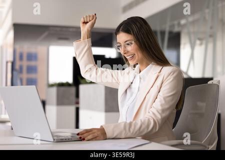 Femme d'affaires excitée célébrant le succès assis au bureau avec ordinateur portable Banque D'Images