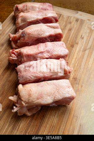 Une rangée de dos de poulet frais et crus coupés en morceaux sur une planche à découper en bois. Gros plan, pas de gens Banque D'Images