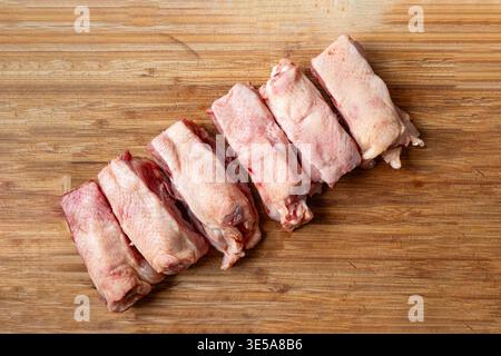 Une rangée de dos de poulet frais et crus coupés en morceaux sur une planche à découper en bois. Gros plan, pas de gens Banque D'Images