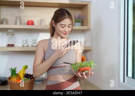 Jeune femme photographiant une salade saine dans une cuisine moderne Banque D'Images