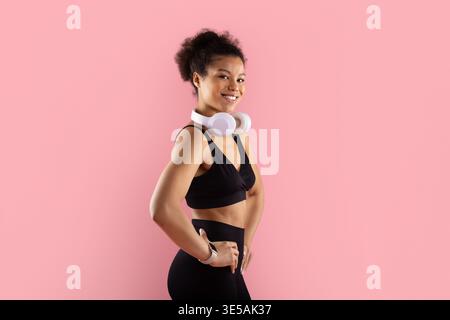 Femme noire athlétique avec des écouteurs autour du cou posant en toute confiance dans les vêtements de sport Banque D'Images
