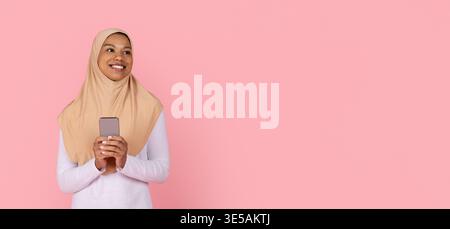 Femme musulmane noire en hijab tenant un smartphone et souriant vers l'espace de copie Banque D'Images