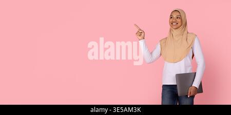 Jeune femme musulmane noire en hijab pointant vers le haut tout en tenant un ordinateur portable Banque D'Images