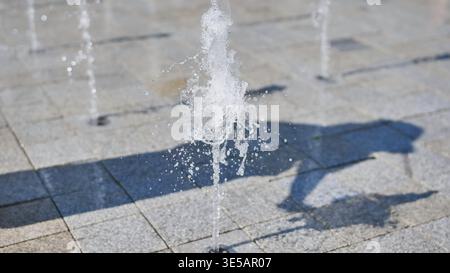 Jets d'eau éclaboussant sur un sol carrelé pour un plaisir rafraîchissant Banque D'Images