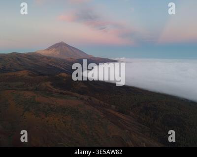 Vue aérienne du mont Teide perçant à travers une mer de nuages, son sommet embrassé par les teintes douces de l'aube, Parc National du Teide, Tenerife, Espagne. Banque D'Images