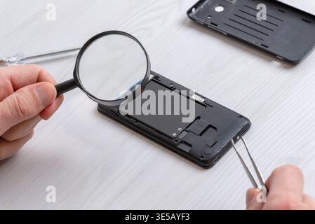 Loupe inspectant les composants internes du smartphone pendant la réparation, mettant l'accent sur les diagnostics, l'analyse matérielle et le dépannage électronique p Banque D'Images