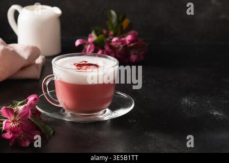 Latte matcha rose avec fleurs de sakura décorées en poudre sur fond noir foncé. Boisson tendance. Sans caféine. Gros plan. Banque D'Images