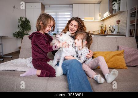 Mère et filles jouant avec un chien de compagnie sur le canapé Banque D'Images