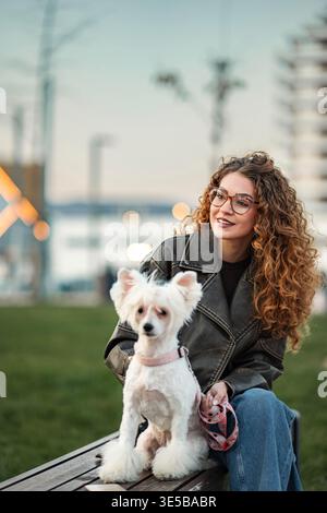 Femme aux cheveux bouclés et chien de compagnie assis sur le banc du parc Banque D'Images