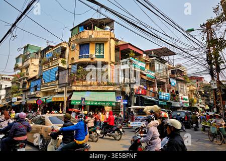 Les motos remplissent une rue animée à Hanoi. Les gens se promènent devant les magasins tandis que les lignes électriques sillonnent au-dessus. La scène montre la vie quotidienne dans la ville. Banque D'Images
