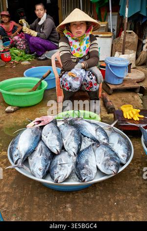 Une femme est assise dans un marché à Phu Quoc, Vietnam, tenant du poisson frais. D'autres personnes sont à proximité, se livrant à des activités liées au marché. Banque D'Images
