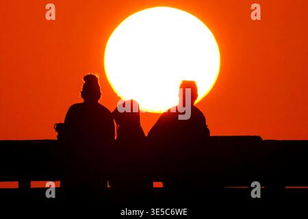 Île de Palms, États-Unis. 01st Apr, 2026. Les gens silhouettés par le lever du soleil regardent la boule orange du soleil grimper au-dessus de l'océan Atlantique depuis la jetée de pêche de Front Beach par un matin de printemps brumeux, le 1er avril 2026 à Isle of Palms, Caroline du Sud. Crédit : Richard Ellis/Richard Ellis/Alamy Live News Banque D'Images
