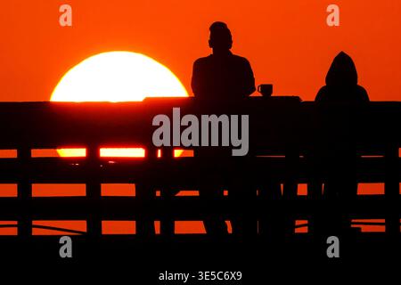 Île de Palms, États-Unis. 01st Apr, 2026. Les gens silhouettés par le lever du soleil regardent la boule orange du soleil grimper au-dessus de l'océan Atlantique depuis la jetée de pêche de Front Beach par un matin de printemps brumeux, le 1er avril 2026 à Isle of Palms, Caroline du Sud. Crédit : Richard Ellis/Richard Ellis/Alamy Live News Banque D'Images