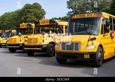 Autobus scolaires jaunes garés dans le parc scolaire avec la flotte de transport alignée pour le ramassage et le dépôt des élèves Banque D'Images