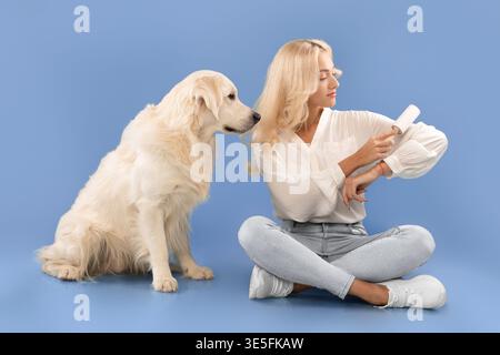 Femme avec Golden Retriever vérifiant sa Smartwatch sur un fond bleu dans un studio Banque D'Images
