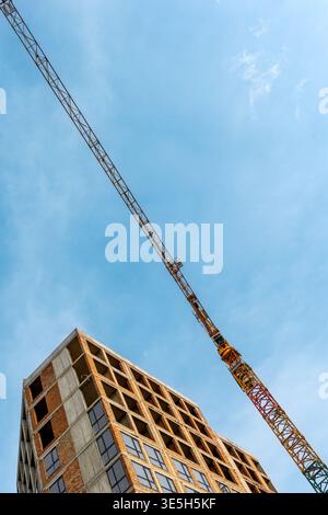 Grue à tour au-dessus d'un immeuble urbain inachevé. Vue en bas angle d'un bâtiment en brique et béton non fini avec une grue à tour, montrant urbain Banque D'Images