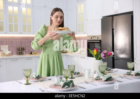 Cadre magnifique. Jeune femme portant une robe mettant une assiette avec des croissants sur la table dans la cuisine Banque D'Images
