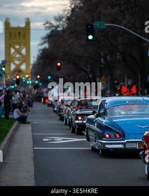 Une rangée de voitures classiques participant à la parade de mardi gras de la Cité des arbres se dirigeant vers le Tower Bridge au crépuscule à Sacramento, en Californie. Banque D'Images