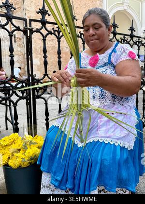 Une femme maya tisse des frondes de palmier dans une décoration traditionnelle à l'extérieur de la cathédrale de Mérida le dimanche des Rameaux à Mérida, Yucatán, Mexique Banque D'Images