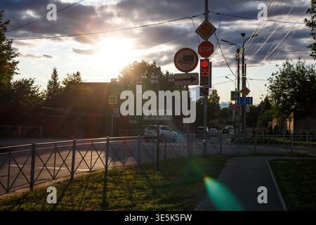 Un coucher de soleil vibrant inonde une intersection russe animée, avec des panneaux routiers clairs, un feu rouge et un ARRÊT bien visible. Lumière dorée cr Banque D'Images