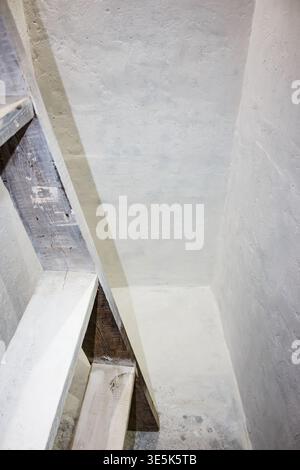 Structure d'escalier en bois rustique dans un sous-sol sombre et blanchi à la chaux avec des murs en béton texturé et un contraste d'ombre sombre Banque D'Images