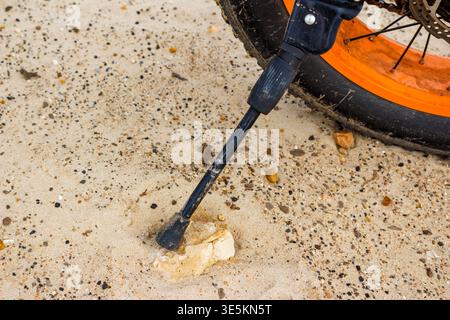 Grimy bike Kickstand soutenant un vélo à gros pneus avec une roue orange vif, reposant sur un sol sablonneux mélangé avec de petits cailloux Banque D'Images