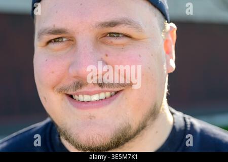 Gros plan portrait d'un jeune homme souriant à l'extérieur dans la lumière naturelle du soleil. Banque D'Images