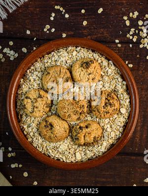 Composition verticale de flocons d'avoine et de biscuits au chocolat dans un bol rustique sur bois sombre, avec de l'avoine dispersée et un espace de copie généreux pour la guérison Banque D'Images