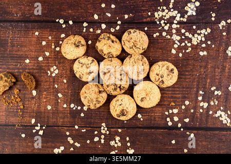 Disposition aérienne de biscuits au chocolat et flocons d'avoine dispersés sur une table en bois rustique avec des miettes et un espace de copie. Collation maison et bre sain Banque D'Images