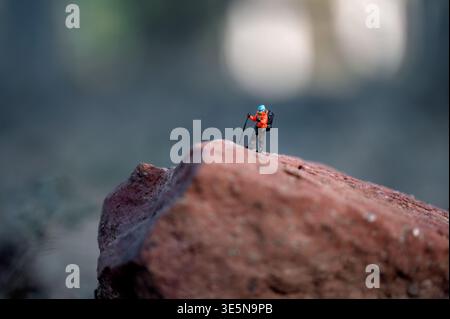 Figurine miniature d'un randonneur avec sac à dos et bâtons de trekking debout sur un grand rocher, symbolisant le défi, l'aventure et surmonter les obstacles Banque D'Images