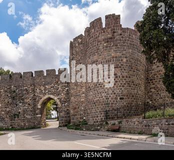 Les anciens murs de pierre du château de Kadifekale et la porte d'entrée voûtée avec une route menant à travers, sous un ciel nuageux à Izmir, Turquie Banque D'Images