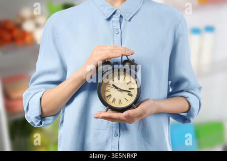 Femme avec réveil dans la cuisine, gros plan. Concept de jeûne intermittent Banque D'Images