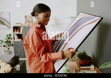 Femme adulte noire positionnant l'impression encadrée pour la promotion décoration intérieure Banque D'Images