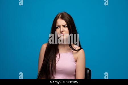 Jeune femme exprimant le doute et la confusion, se sentant sceptique ou questionnant sur un fond bleu de studio Banque D'Images