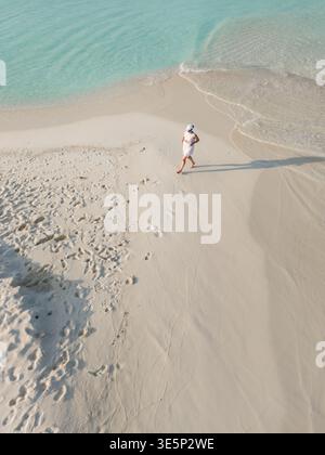 Vue aérienne d'une plage tranquille où les eaux turquoises rencontrent le sable blanc immaculé, avec une figure solitaire se promenant le long du rivage, Dhidhdhoo, Maldives Banque D'Images