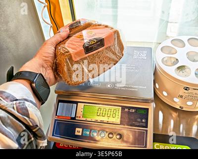 Orenburg, Russie - 22 août 2025 : une personne pèse une miche de pain à l'aide d'une balance dans la zone de caisse d'un supermarché tout en faisant ses courses Banque D'Images