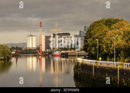 Le grand voilier Glenlee amarré devant le Riverside transport Museum sur la rivière Clyde, encadré par des bâtiments modernes en bord de mer, des arbres d'automne et des refle calmes Banque D'Images