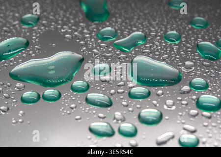 Des gouttelettes vertes s'accrochent à une surface lisse et réfléchissante. Les perles d'eau brillent sous un éclairage doux et diffus. De minuscules gouttelettes se dispersent à travers un cool, métallique Banque D'Images